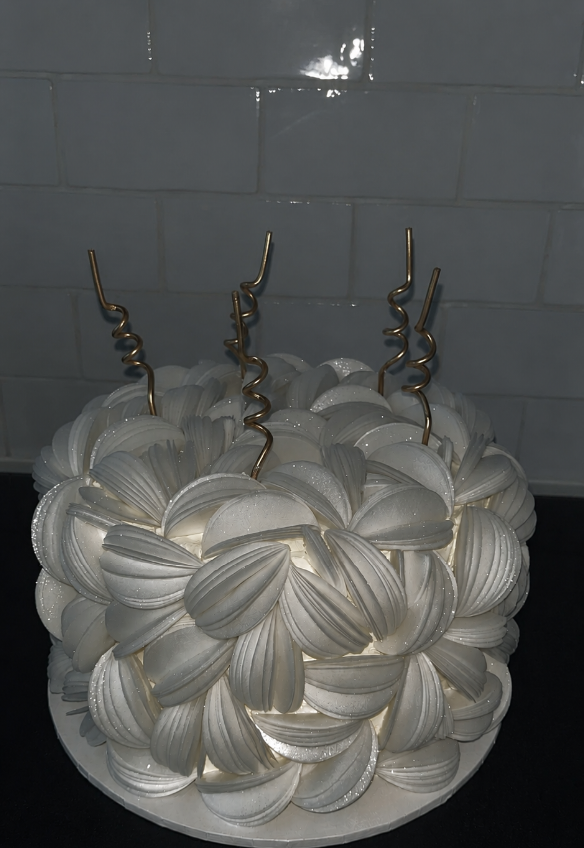 A white petal-textured celebration cake with gold swirl candles, made by The Cake Cove